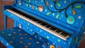 Photo of The Corner Public Piano at 941 Main Campus Dr, Raleigh, NC 27606. A cobalt-blue student-painted public piano on the main stage at The Corner, NC…